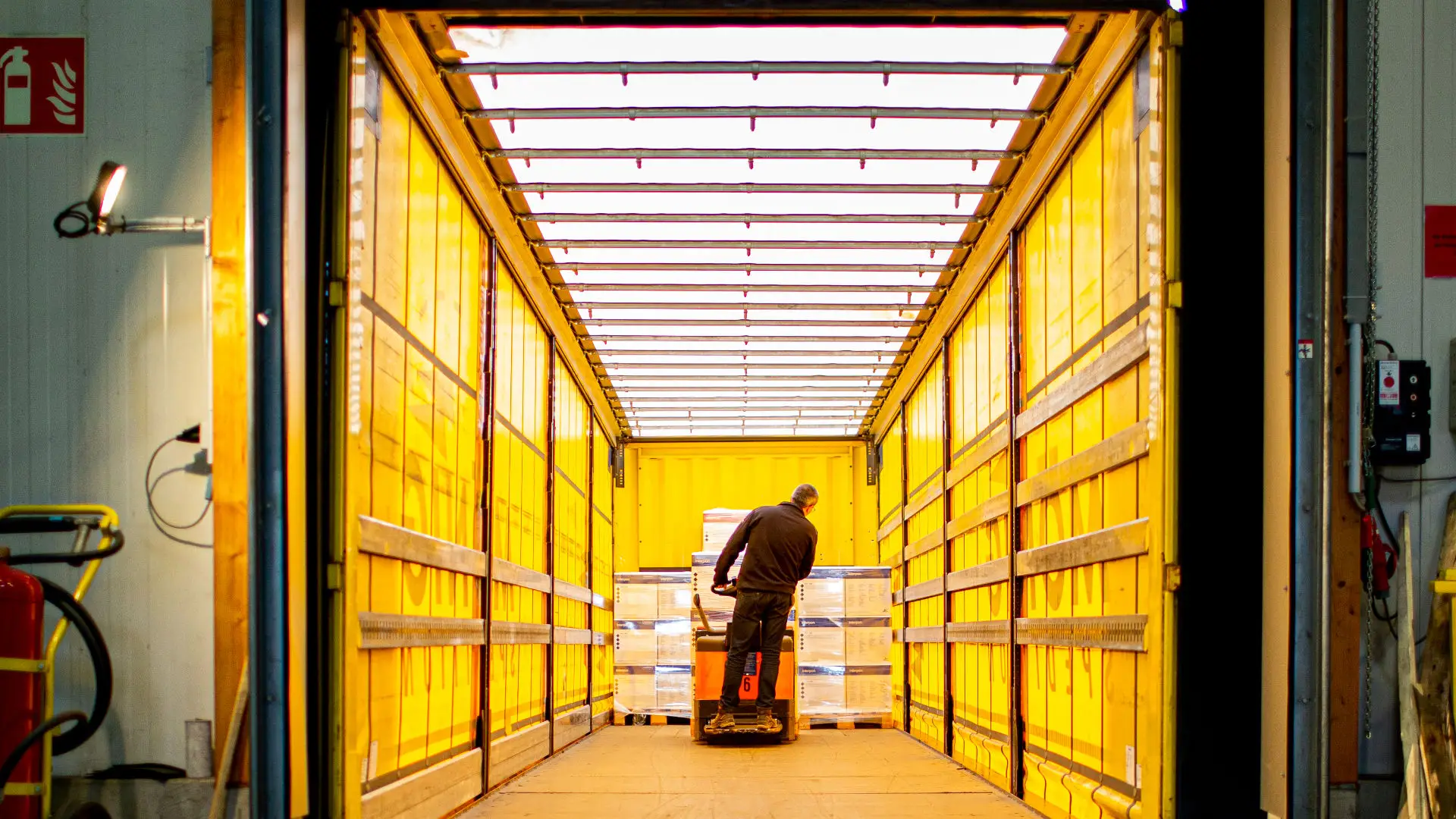 Innenansicht eines gelben LKW von Mönig. Ein Mitarbeiter belädt den LKW mit Waren mithilfe eines Gabelstaplers